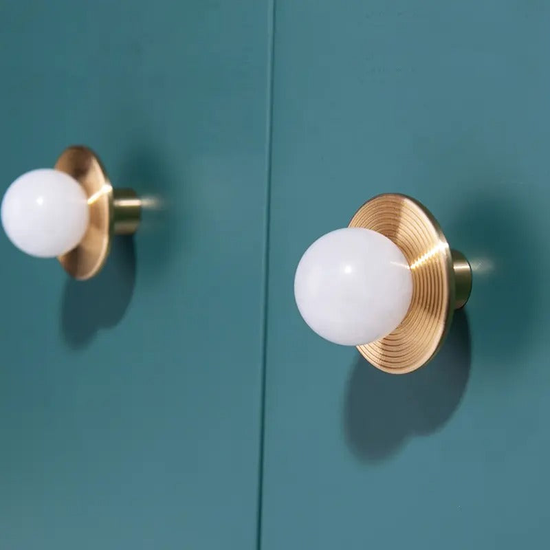 Gold door handles with white knobs mounted on a teal door, offering a bold and elegant contrast by Mantara.