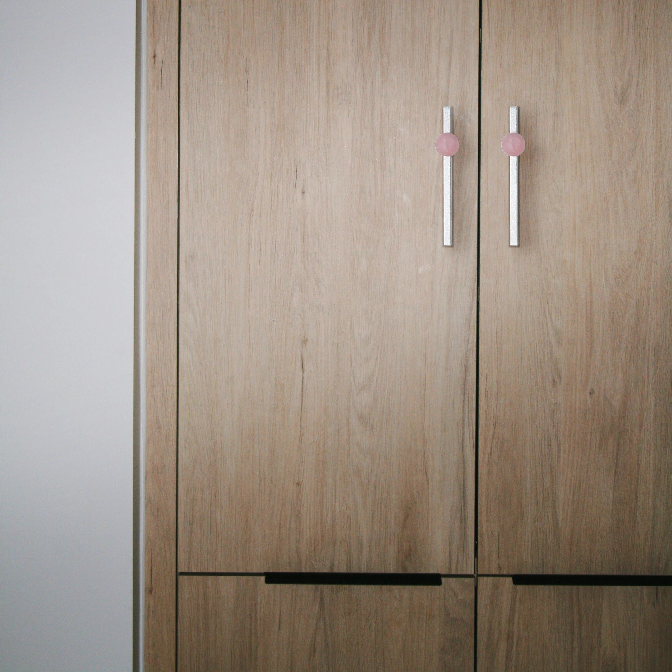 Wooden wardrobe with pink and silver handles placed against a neutral background, offering a modern touch by Mantara.