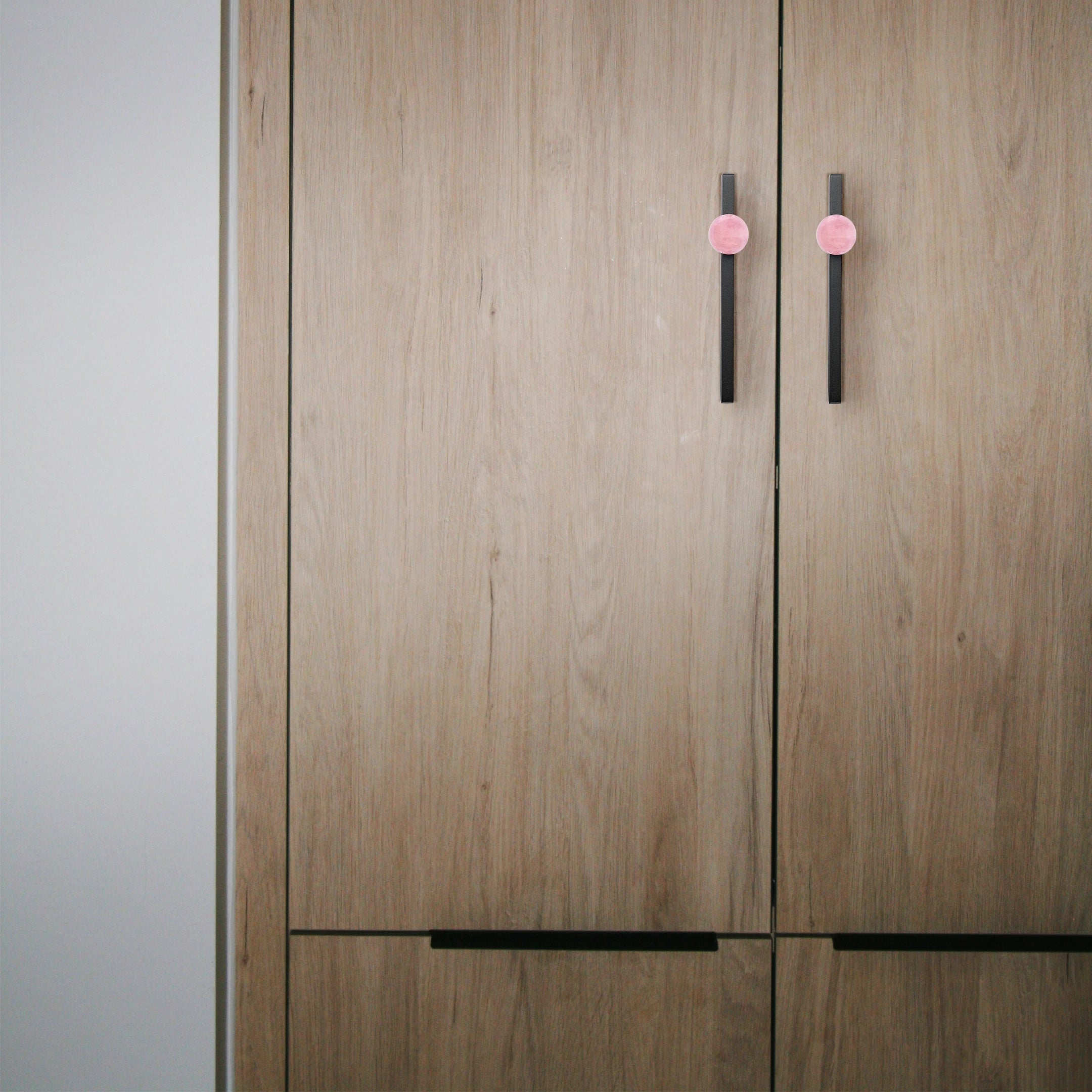 Wooden wardrobe with pink and black handles set against a neutral background, blending charm and contrast by Mantara.