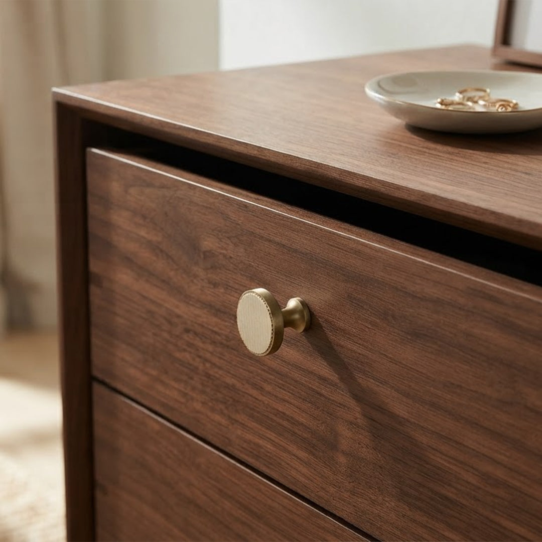 A close-up of a dark brown wooden nightstand or dresser drawer with a round brass knob, featuring a small ceramic dish on top.