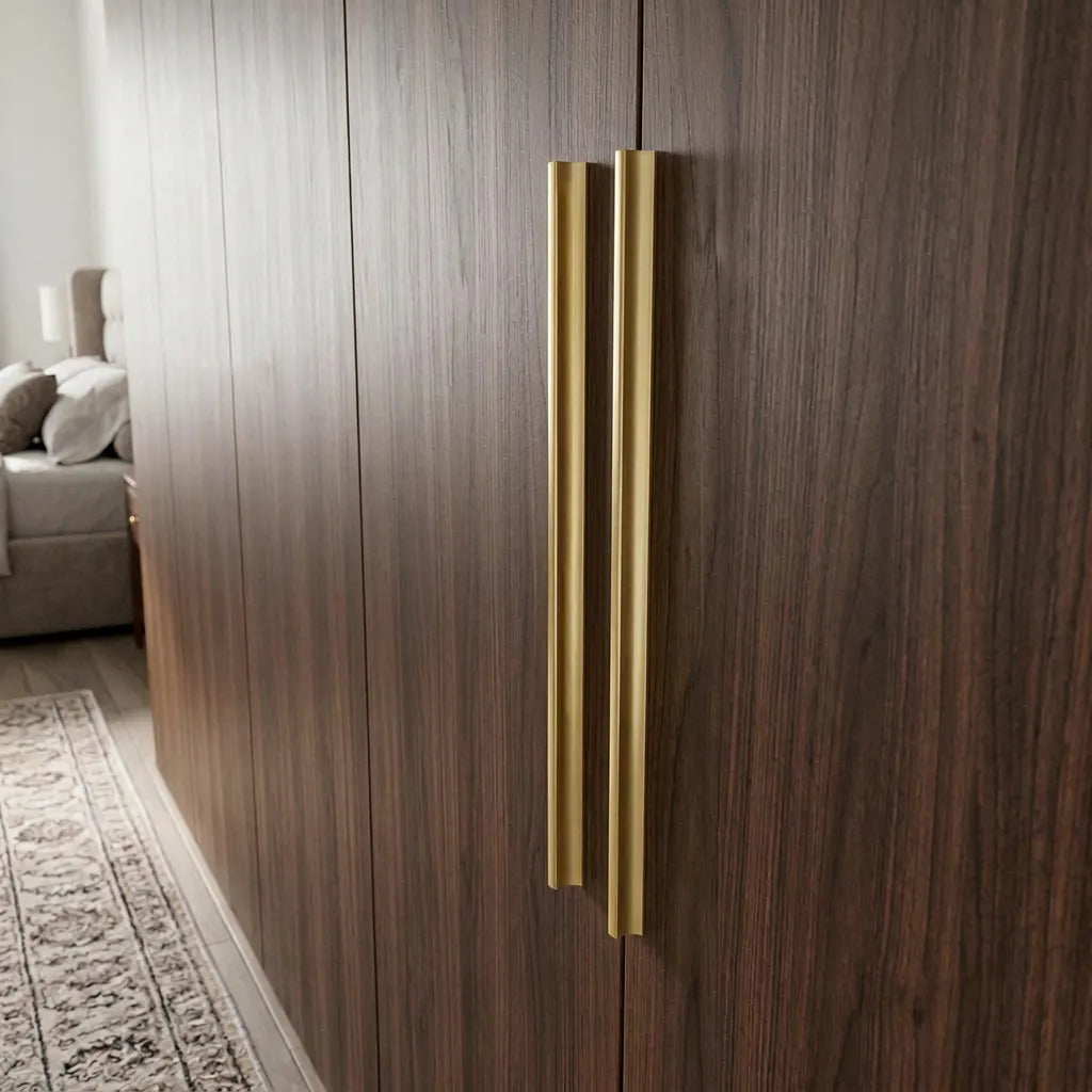 Two slim vertical brushed gold handles mounted on dark brown wood grain cabinet doors in a modern interior setting.