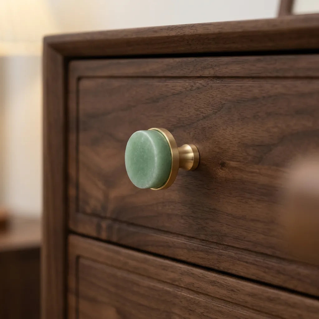 A close-up of a dark wood dresser drawer featuring a round, light green velvet knob with a brushed brass metal base.