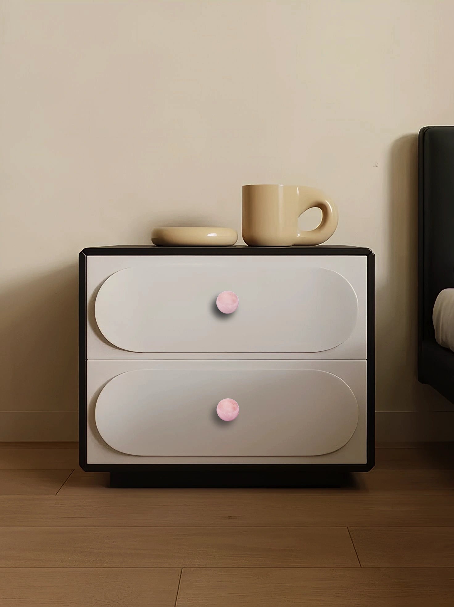 Modern nightstand with two drawers and pink knobs, topped with a cup and saucer, adding charm and style by Mantara.