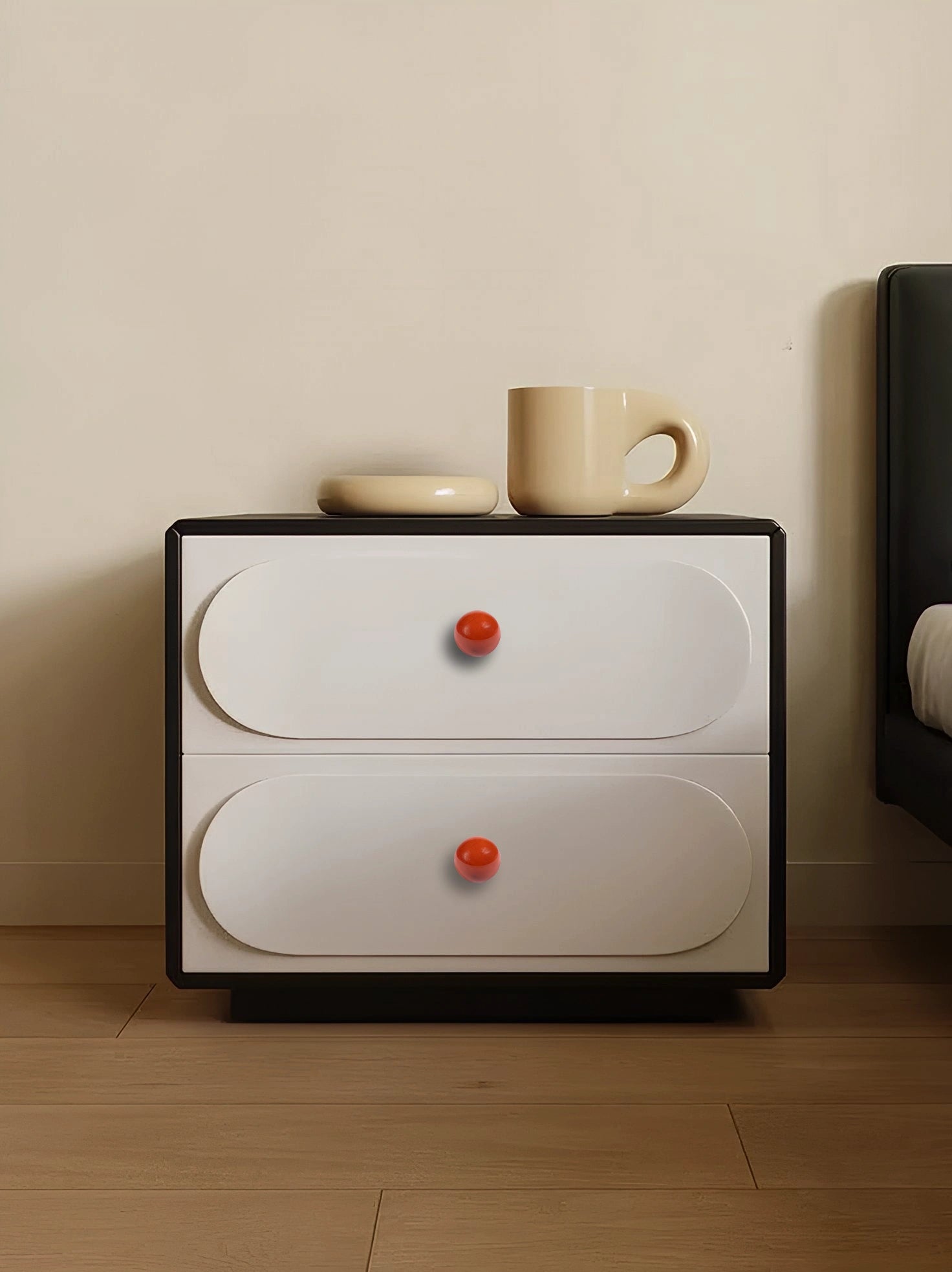 Small nightstand with two drawers and red knobs, topped with a cup and saucer, offering a cozy look by Mantara.