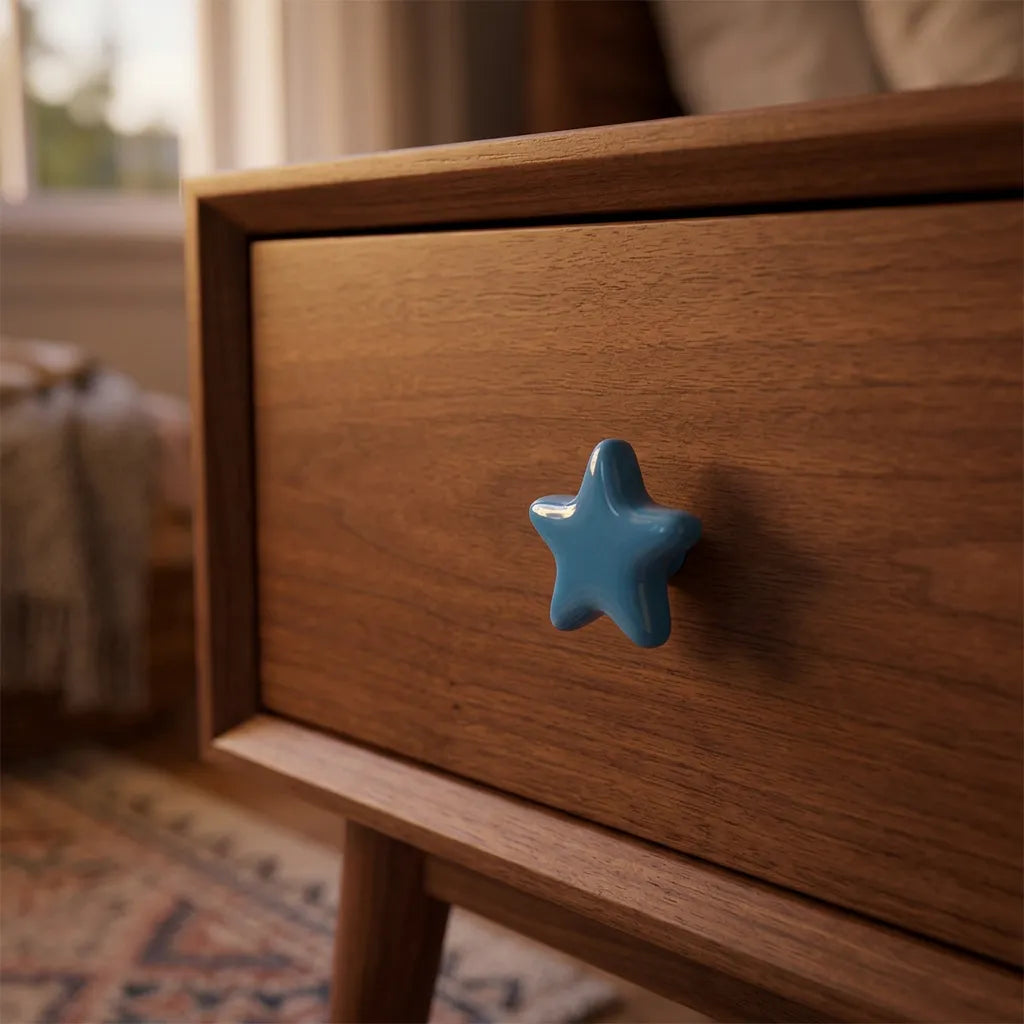 A close-up of a wooden nightstand drawer featuring a glossy, five-pointed star-shaped blue knob, set in a softly blurred bedroom environment.