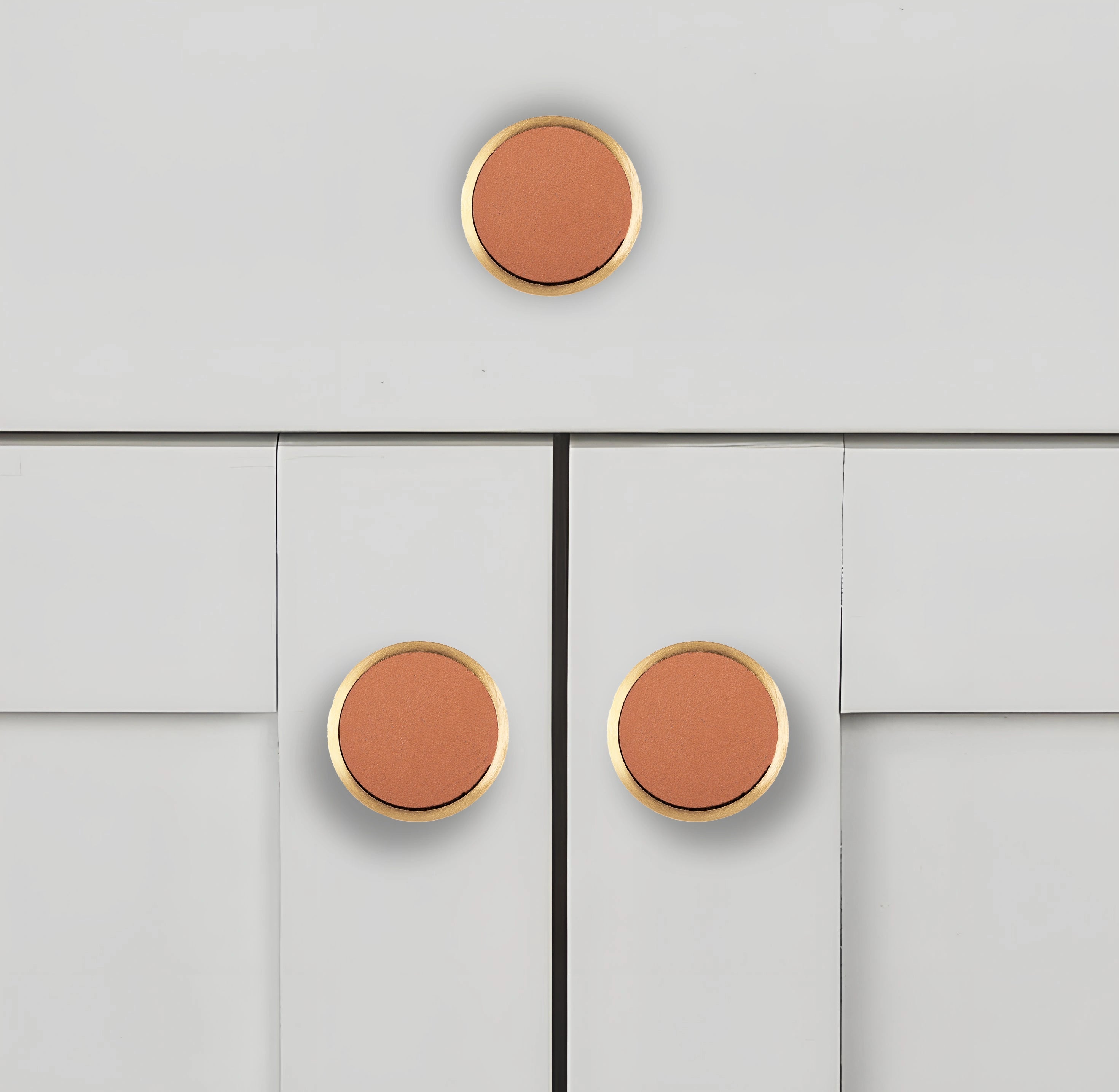 Leather knobs with gold trim mounted on a light gray cabinet, adding a warm, modern accent to the design by Mantara.