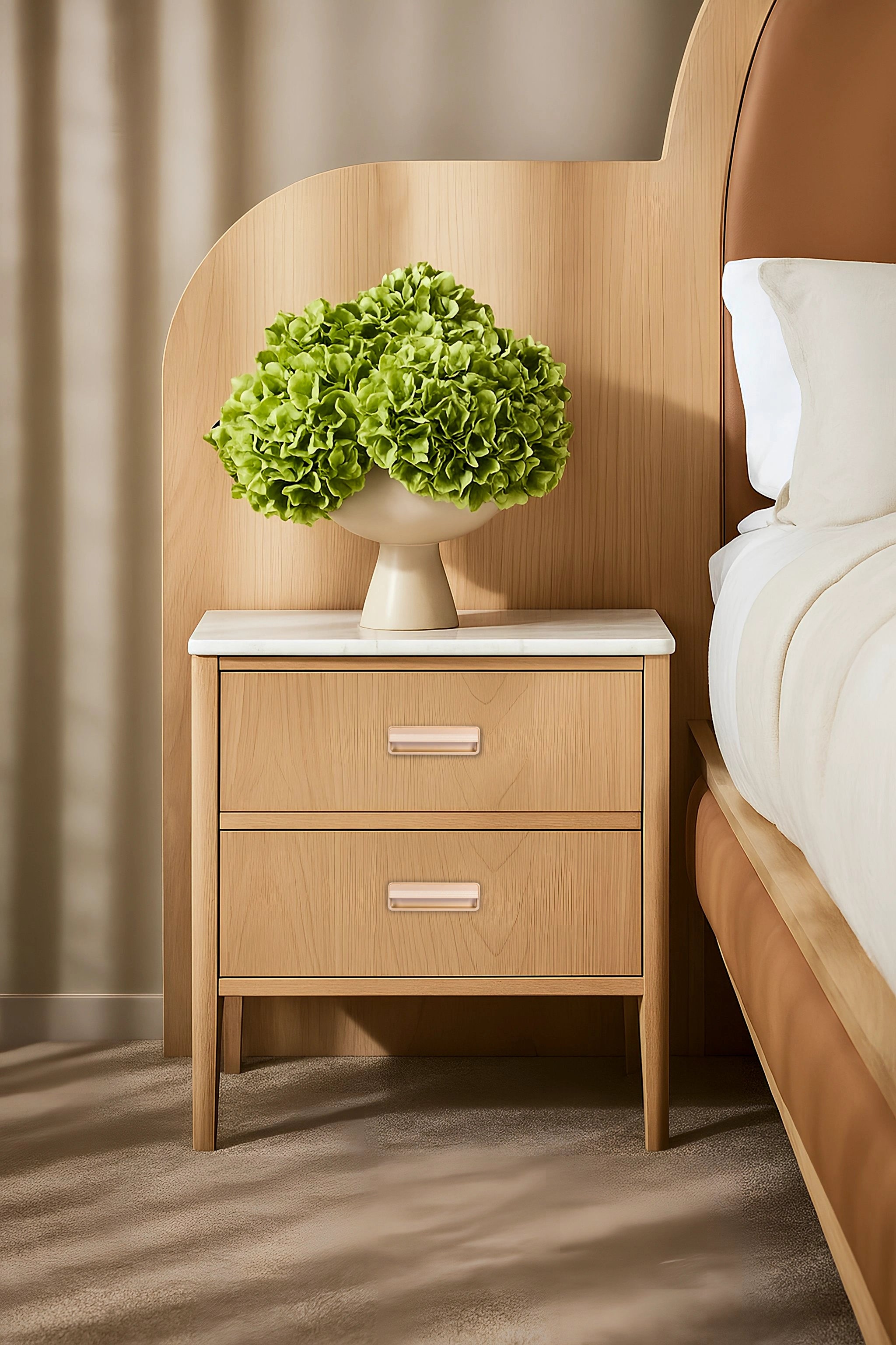 Wooden nightstand with a white marble top and sleek handle, styled with green flowers in a vase next to a bed—by Mantara.