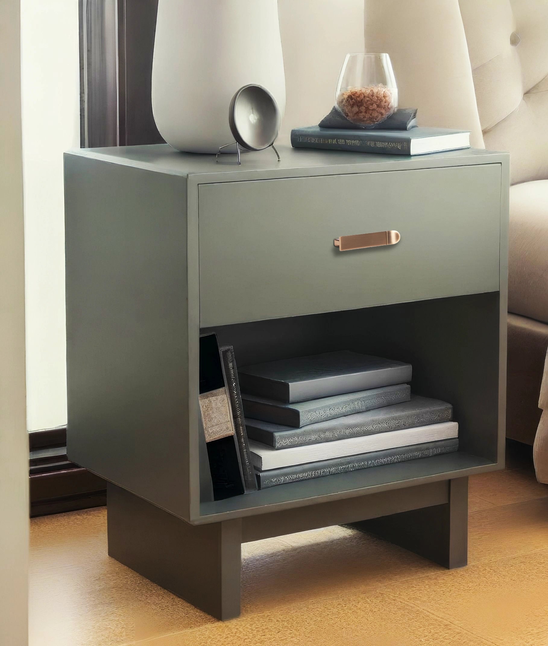 Gray nightstand with a drawer featuring a sleek handle and an open shelf, styled in a cozy room setting—by Mantara.