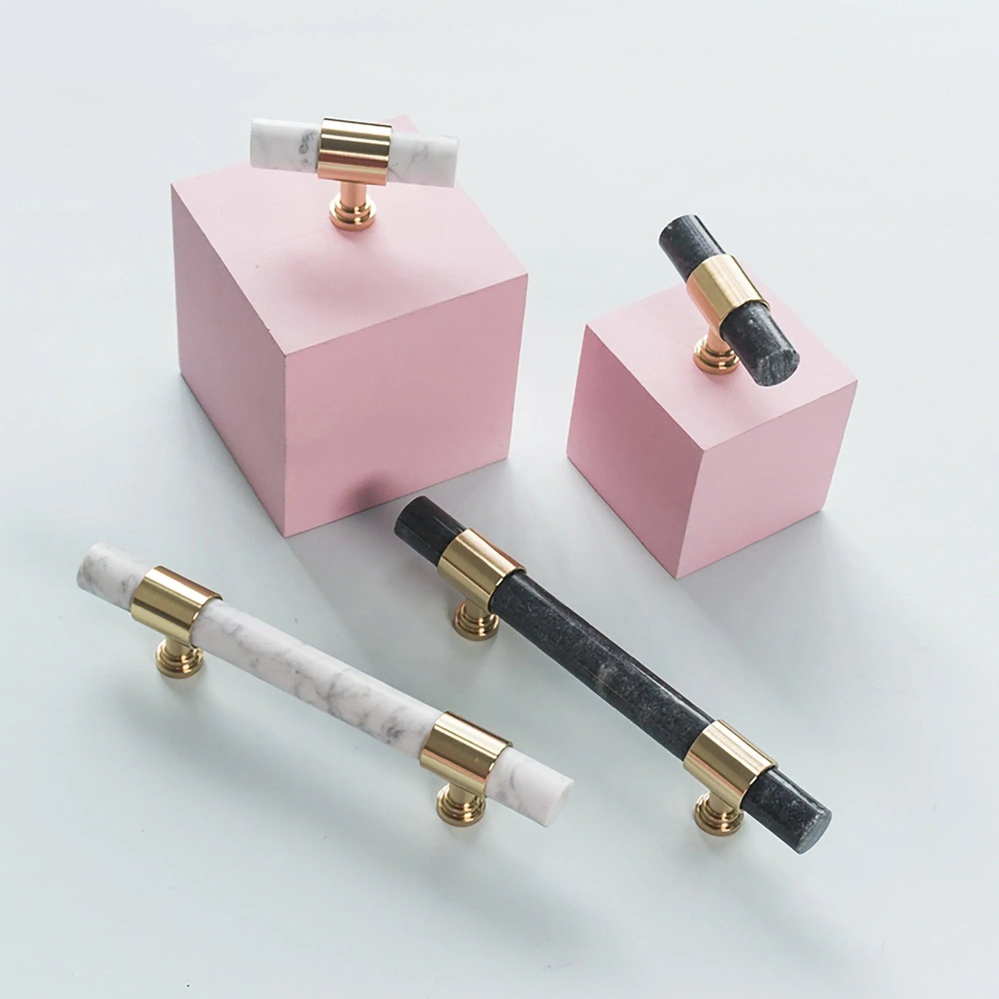 A collection of Arabella T Bar Handles in various colours, including black, gold, white, and grey, displayed on a pink background, designed by Mantara