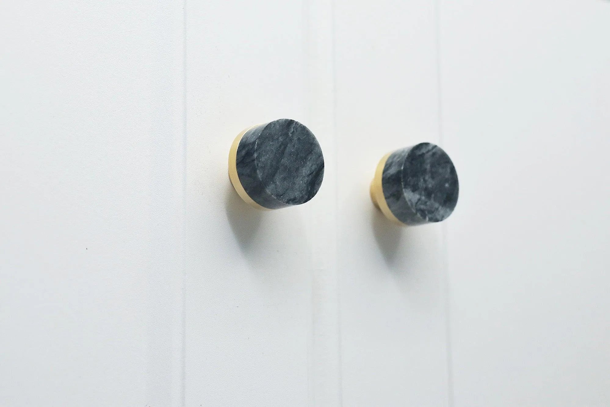 Two black and gold marble knobs mounted on a white wall, adding a refined and elegant accent to the space by Mantara.