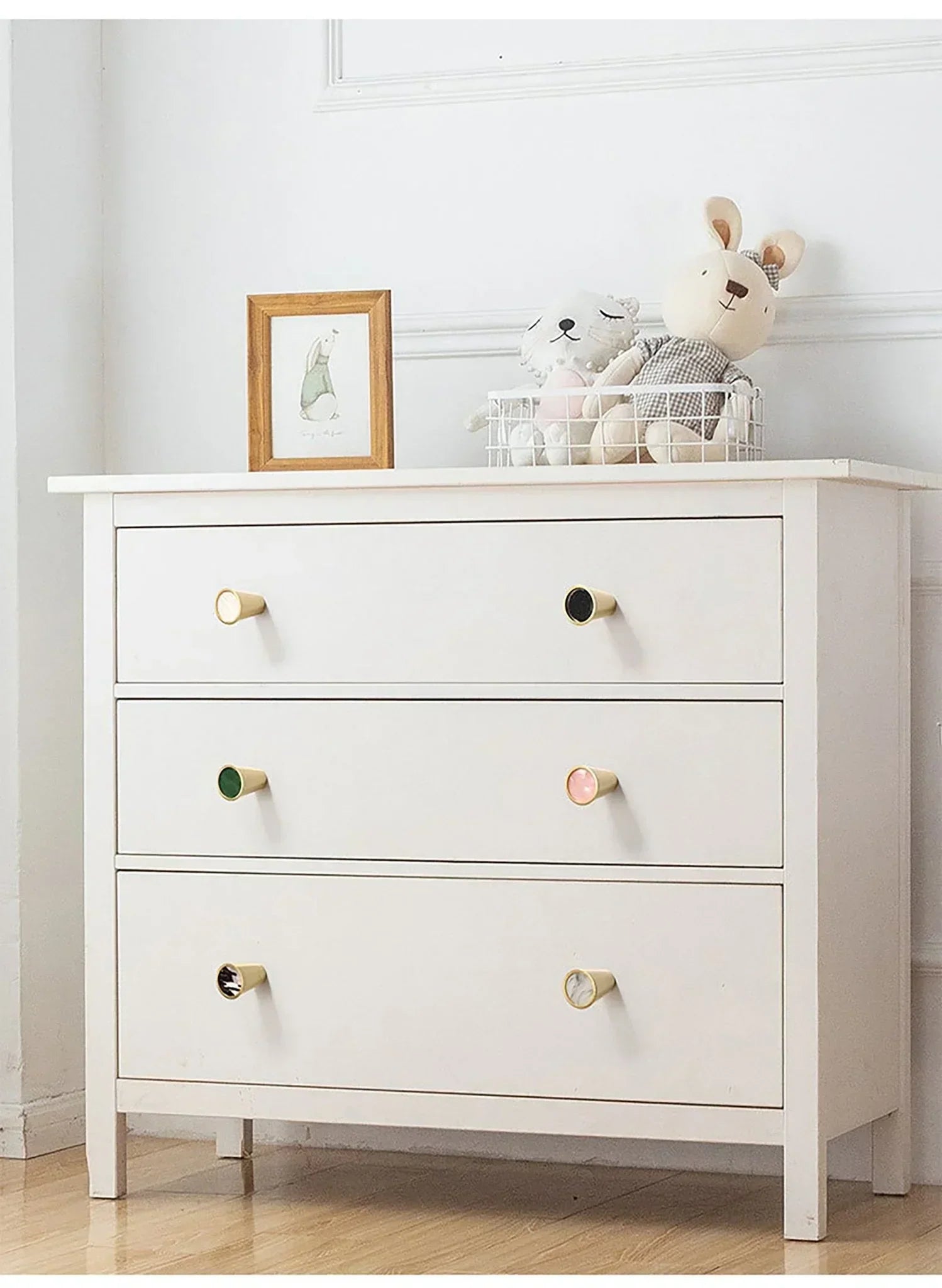 White dresser with colorful knobs in a room with toys and a picture frame.
