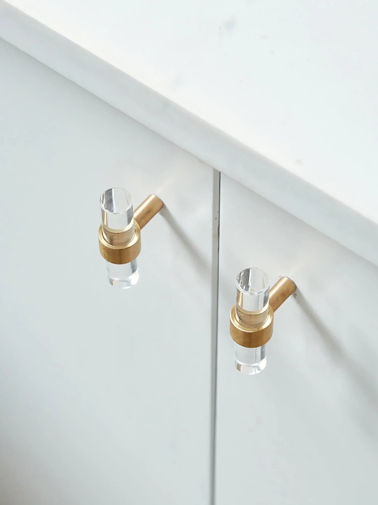 A sleek T-bar handle, Petra II made of clear acrylic with brushed brass supports in transparent white finish, model A-0008 by Mantara, A-0008.