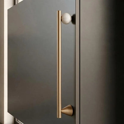 A modern long bar cabinet handle in brushed brass with a spherical white knob, mounted on a dark charcoal-gray door.