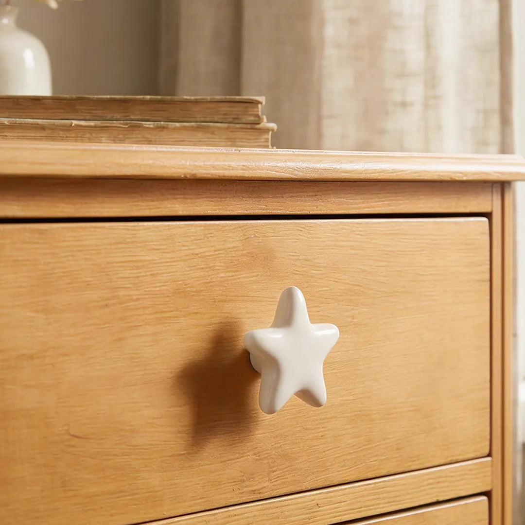A close-up of a light natural wood dresser drawer featuring a glossy white star-shaped ceramic knob.