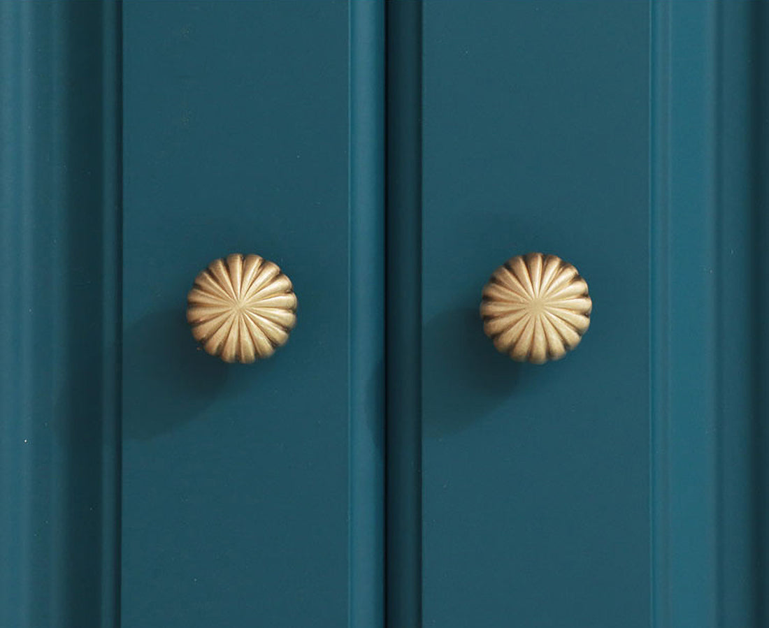Two gold cabinet knobs on a teal cabinet door