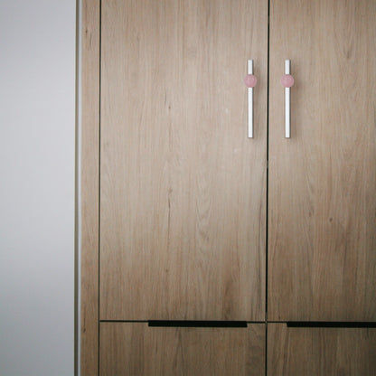 Wooden wardrobe with pink and silver handles placed against a neutral background, offering a modern touch by Mantara.