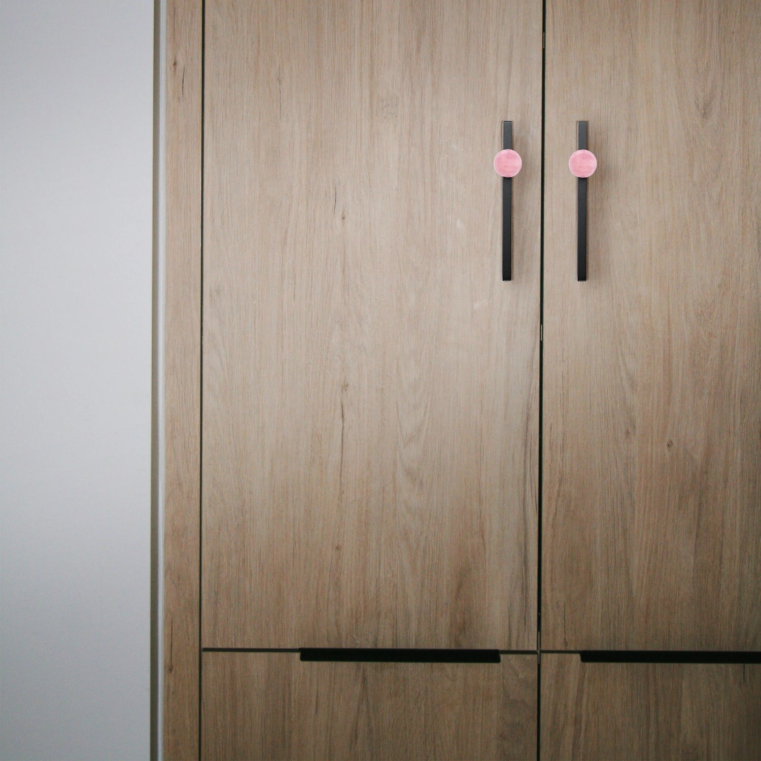 Wooden wardrobe with pink and black handles set against a neutral background, blending charm and contrast by Mantara.