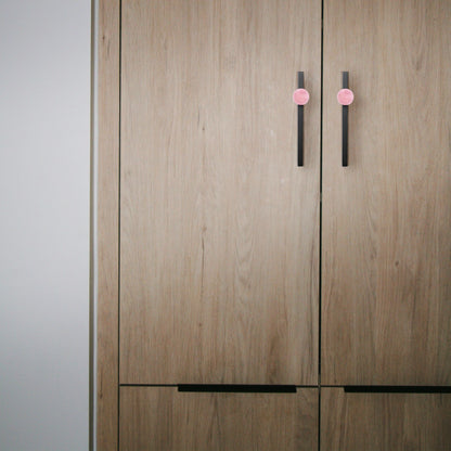 Wooden wardrobe with pink and black handles set against a neutral background, blending charm and contrast by Mantara.