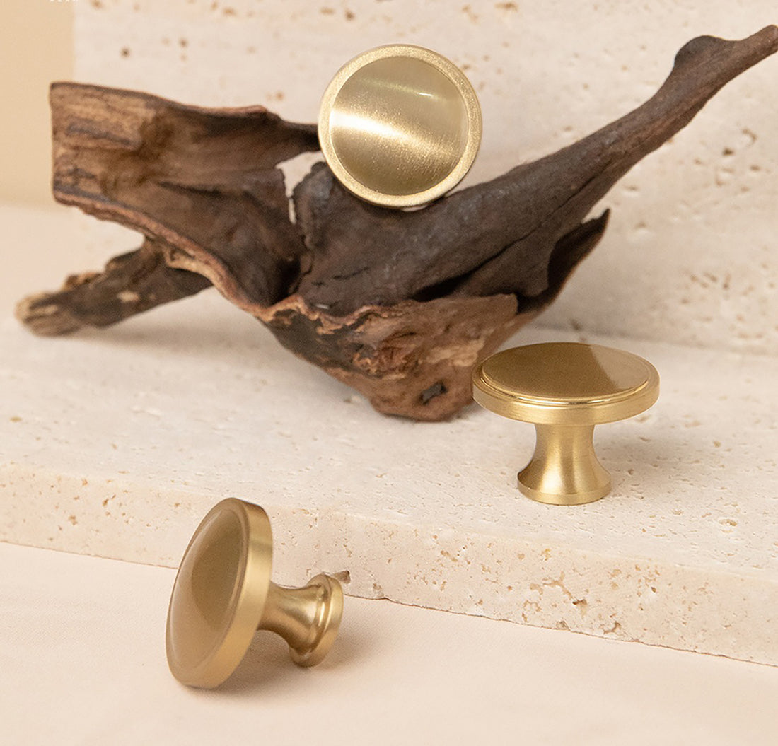 Gold cabinet knobs on a textured surface with a piece of driftwood.