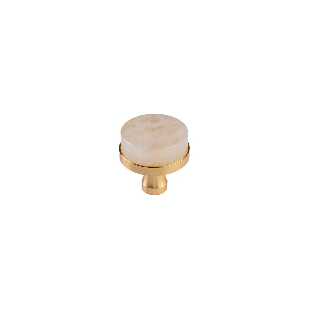 A single round cabinet knob featuring a polished cream-colored stone top with subtle crystal, mounted on a brushed gold brass