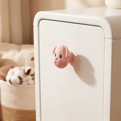 A small pink dog-shaped cabinet knob attached to a white storage cabinet in a softly lit room, with a woven basket and plush toy blurred in the background.