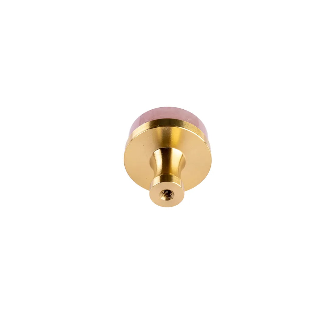 A round gold metal knob or pull with a pinkish-red translucent top cap, shown against a plain white background.