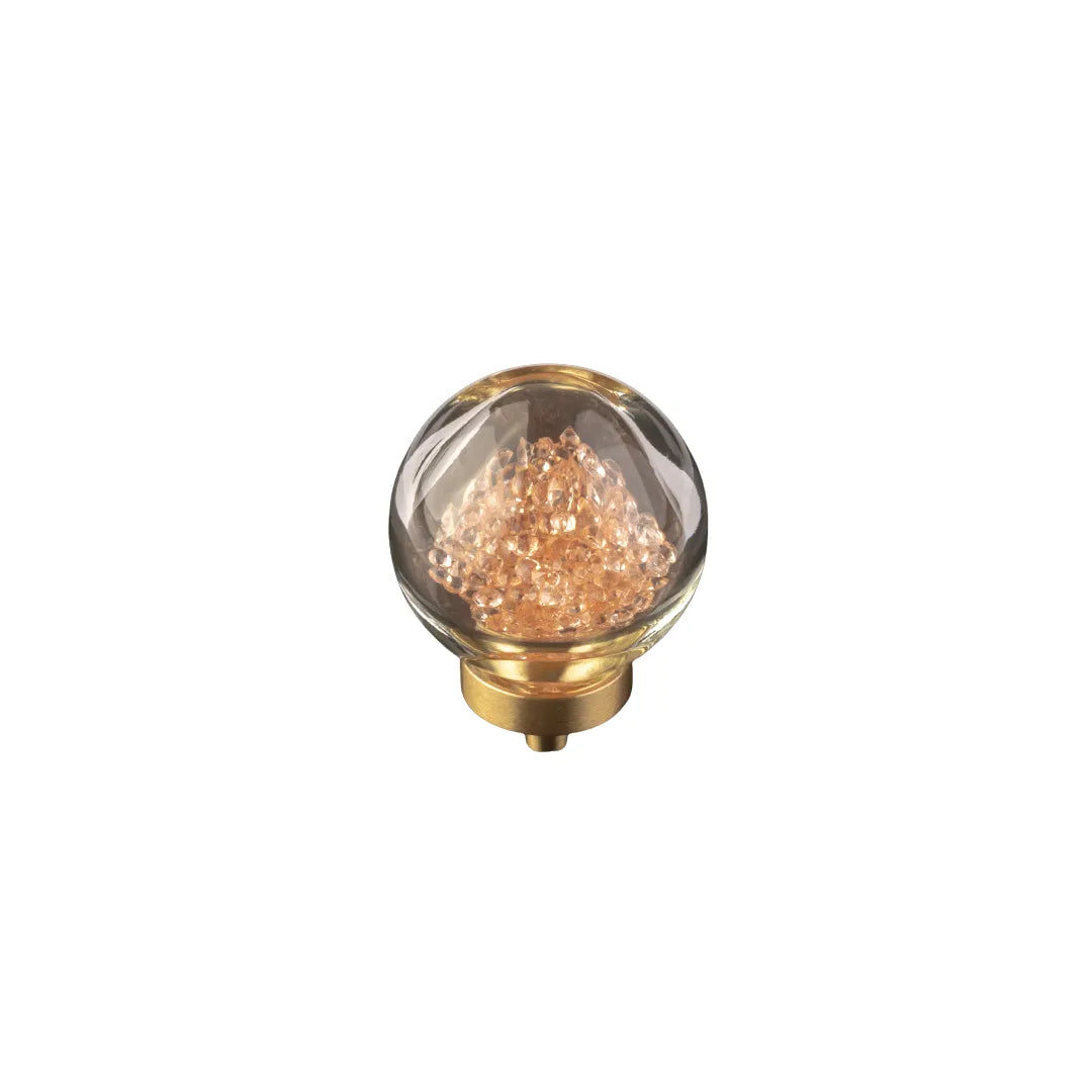 A decorative glass globe light bulb with a gold-toned metal base, filled with shimmering rose-gold or copper-colored crystals, shown on a plain white background.