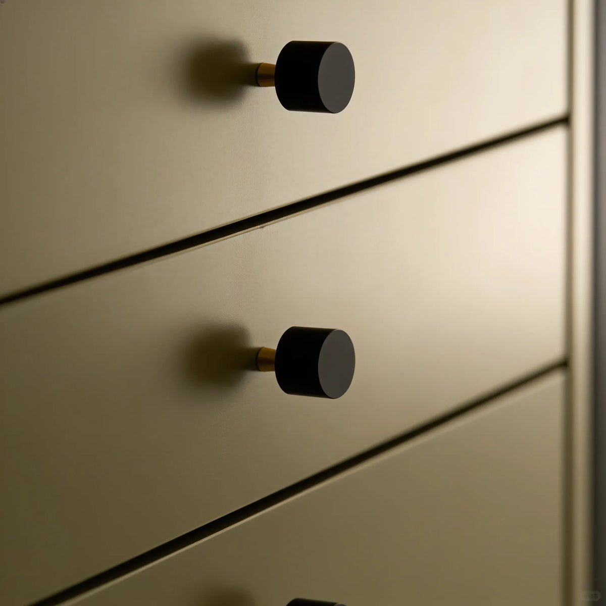 Close-up of a modern dresser or cabinet with matte black round knobs and a warm brushed brass or gold-toned metal finish.