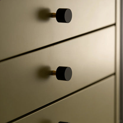 Close-up of a modern dresser or cabinet with matte black round knobs and a warm brushed brass or gold-toned metal finish.