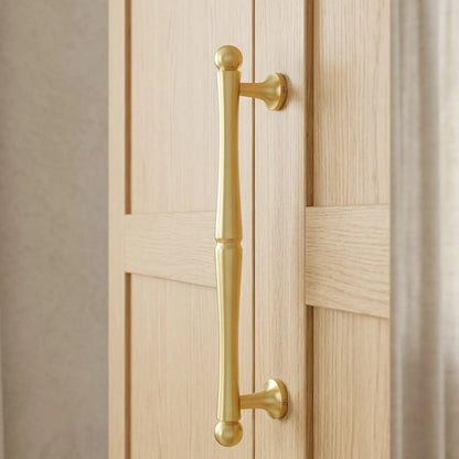 A polished brass door handle with a classic bar design and ball finials, mounted on a light oak paneled door.