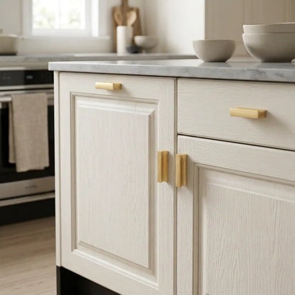 Cream-colored kitchen cabinets with light wood handles, featuring a white marble countertop in a bright kitchen setting.