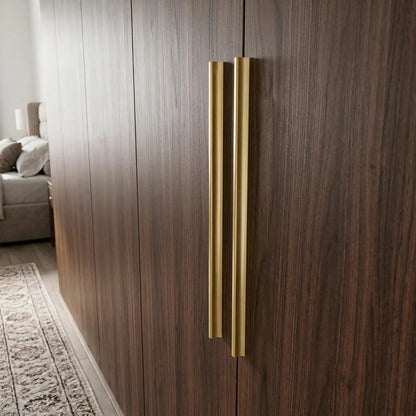 Two slim vertical brushed gold handles mounted on dark brown wood grain cabinet doors in a modern interior setting.
