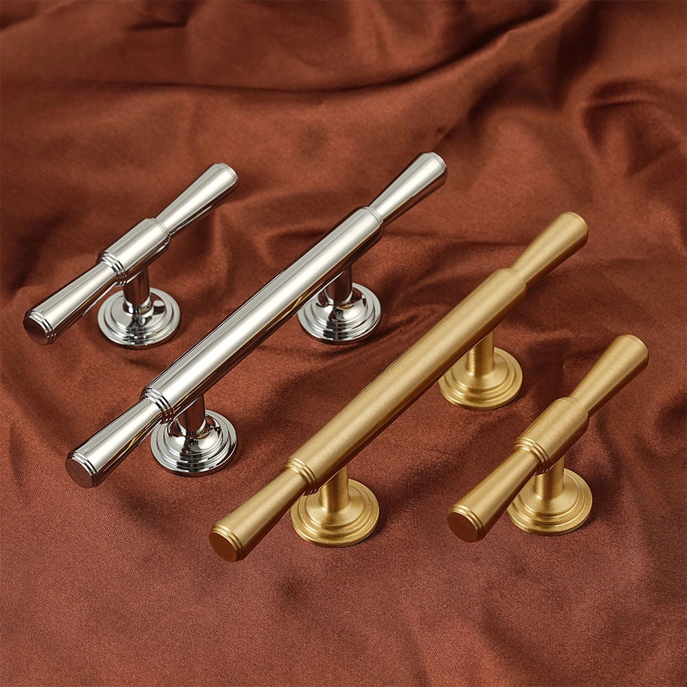 Four cabinet knobs and pulls in polished silver and brushed gold finishes, arranged on draped rust-brown fabric.