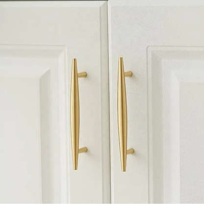 Two white cabinet doors with sleek, vertical, gold handles. The handles are elongated and modern, adding a touch of elegance to the minimalist design.