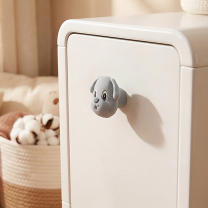 A small grey dog-shaped cabinet knob attached to a white storage cabinet in a softly lit room, with a woven basket and neutral decor blurred in the background.