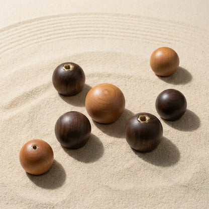Seven wooden zen stones of varying sizes and tones, including light brown, medium tan, and dark brown, arranged on a bed of raked sand.