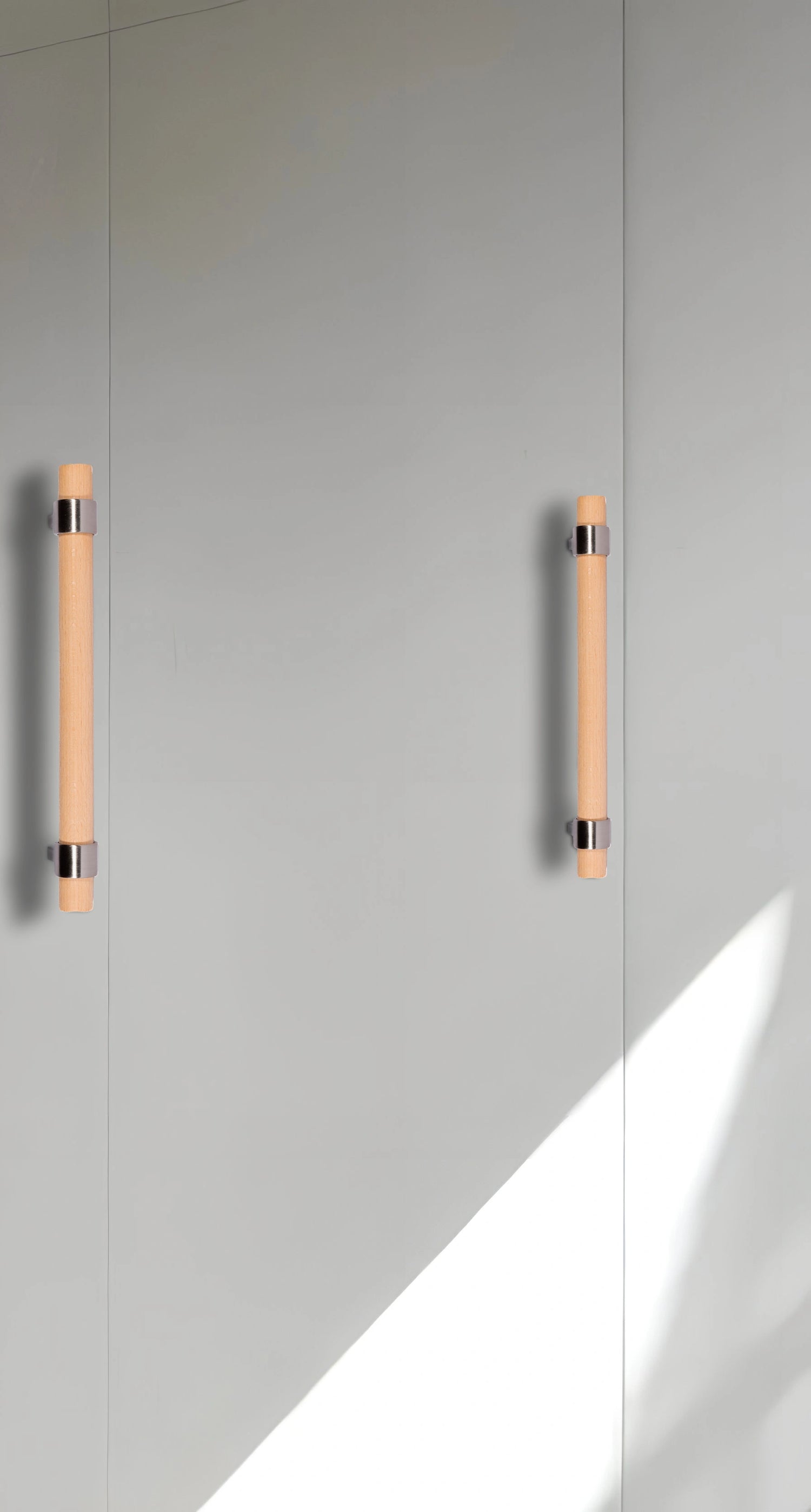 Modern cabinet handles mounted on a light gray door, showcasing clean lines and subtle contrast—designed by Mantara
