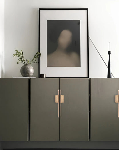 Modern interior with a dark green cabinet featuring sleek handles, framed abstract art, and a vase with greenery—by Mantara.