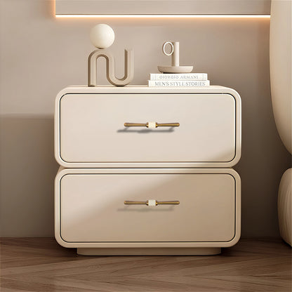 Beige nightstand with two drawers and Bronze handles, styled with decorative items on a wooden floor—by Mantara.