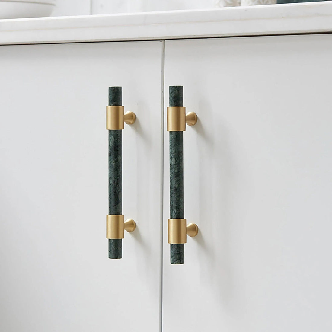 Pair of Arabella handles on a white cabinet—one vertical in green, one horizontal in brass—showcasing bold style by Mantara.