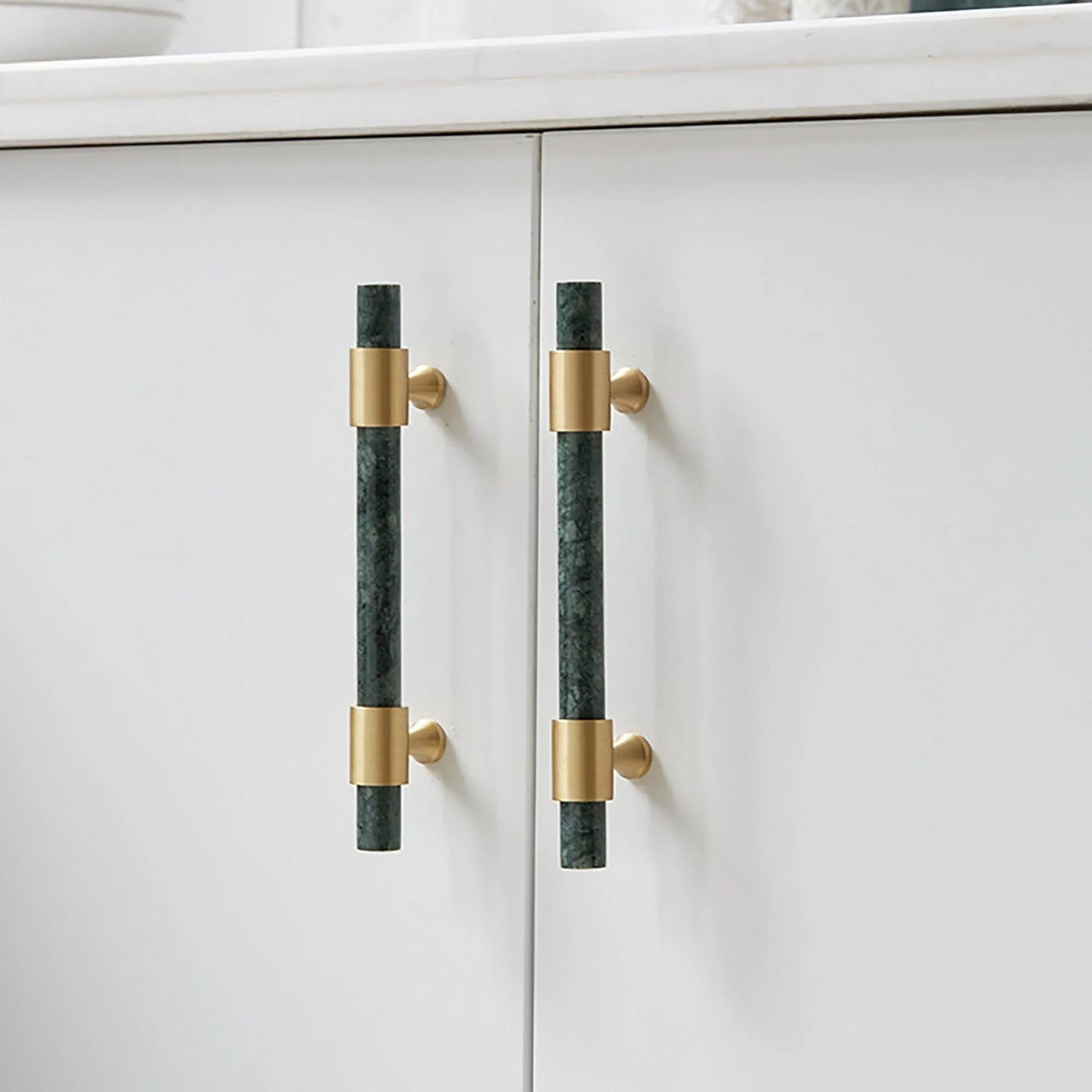 Pair of Arabella handles on a white cabinet—one vertical in green, one horizontal in brass—showcasing bold style by Mantara.