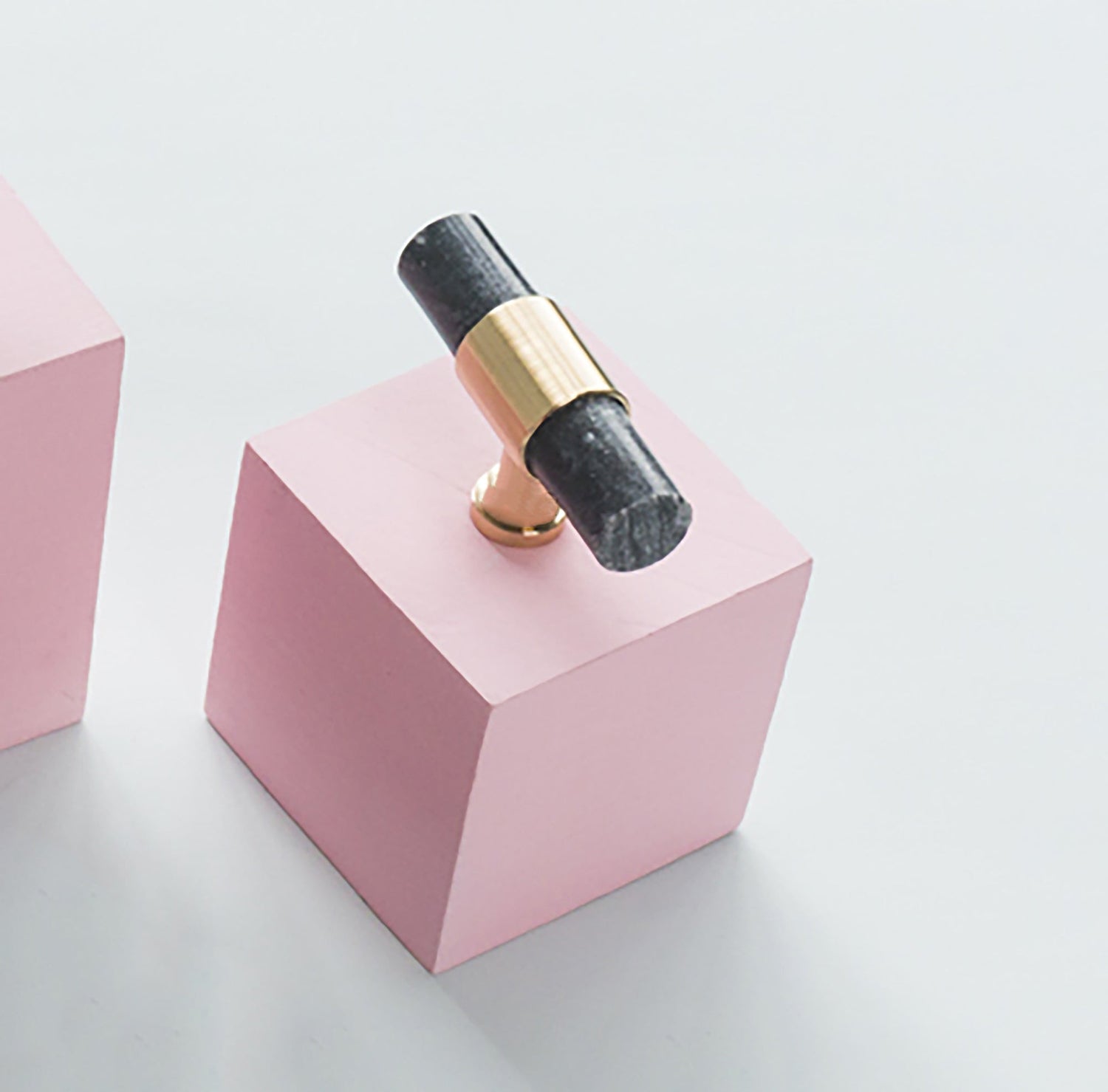 Black and gold ring on a pink geometric block against a light gray background, designed by Mantara