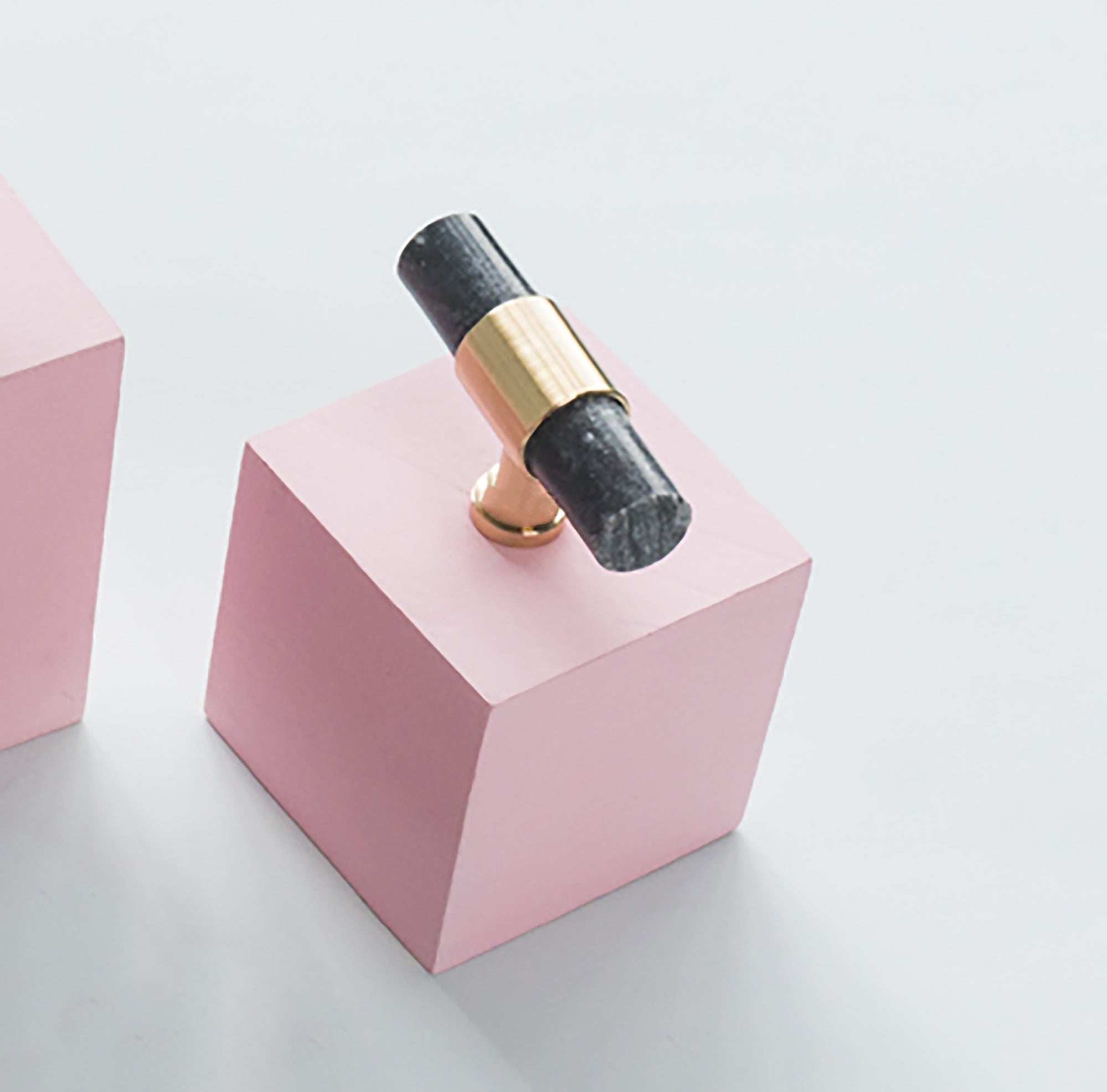Black and gold ring on a pink geometric block against a light gray background, designed by Mantara