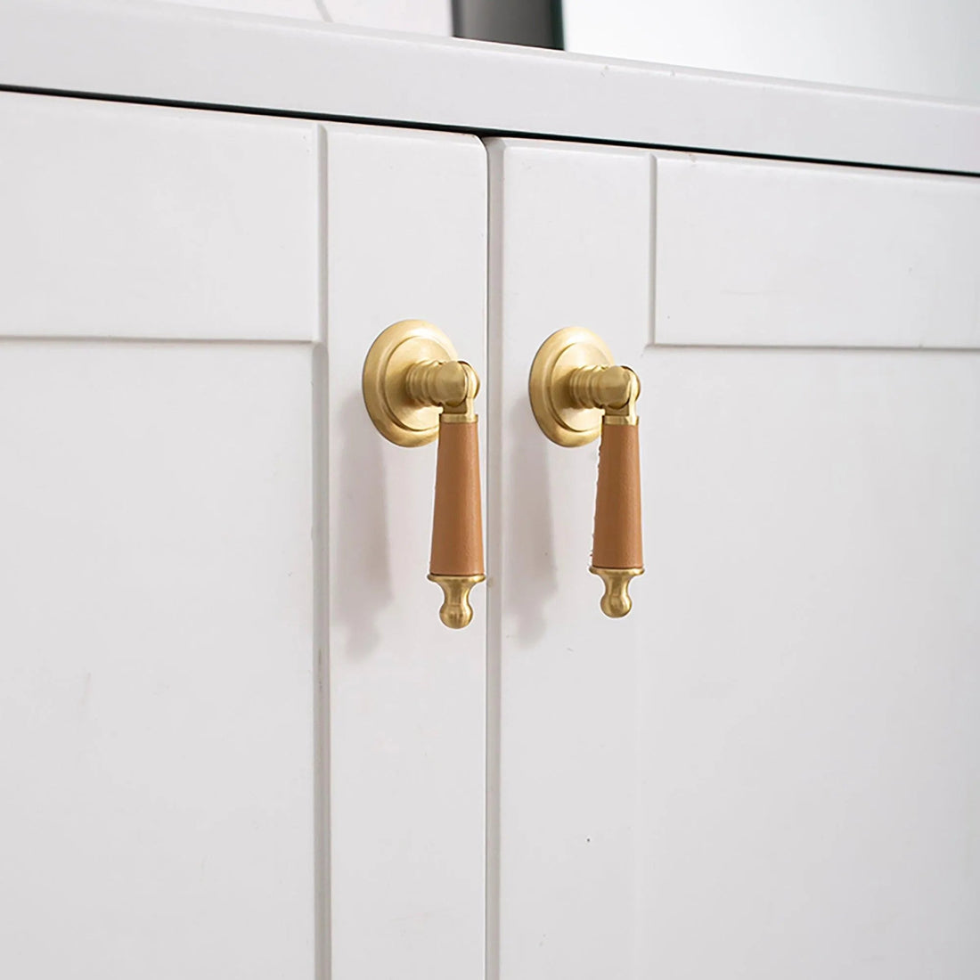 Gold-colored drop knob mounted on a white cabinet door, offering a simple yet elegant hardware detail by Mantara