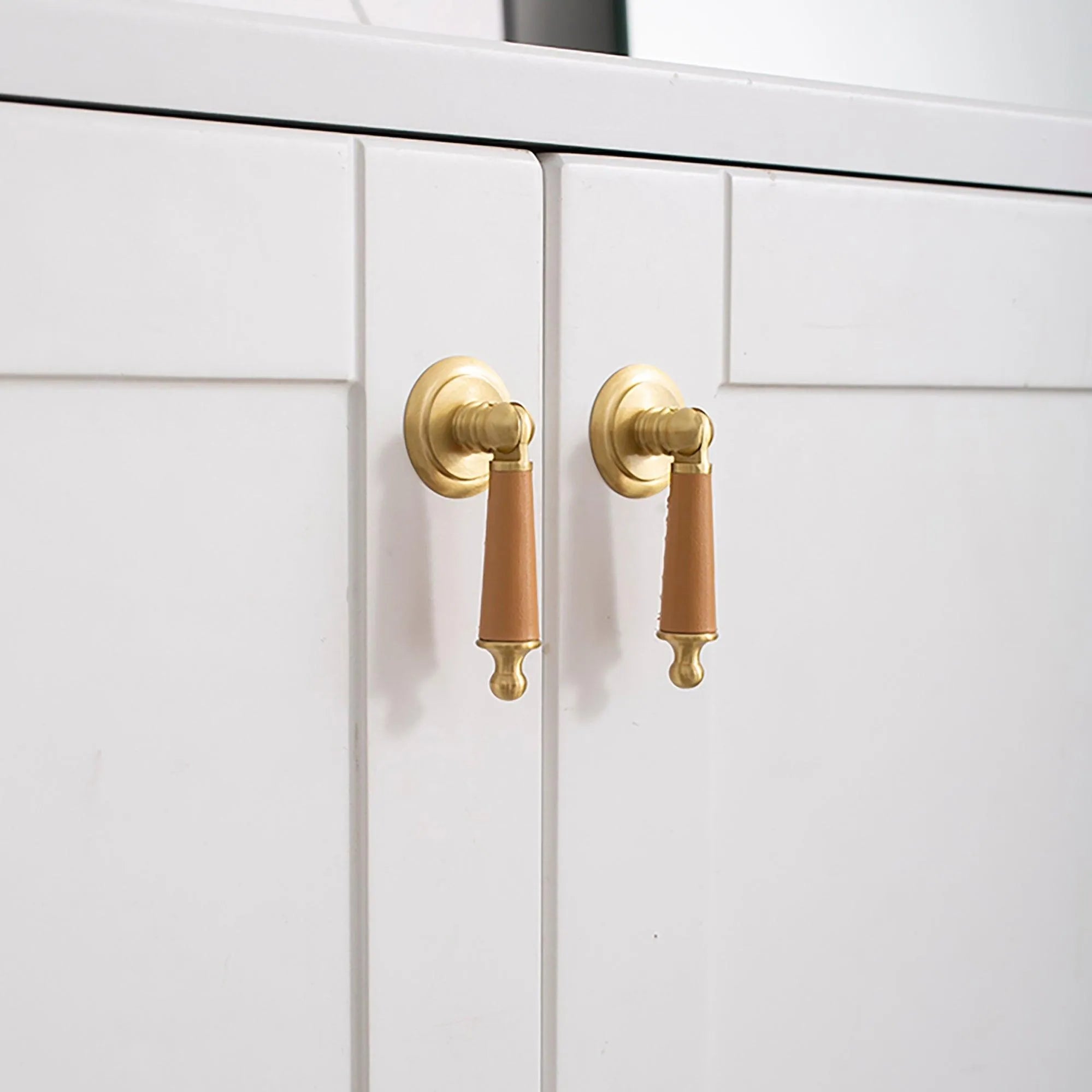 Gold-colored drop knob mounted on a white cabinet door, offering a simple yet elegant hardware detail by Mantara