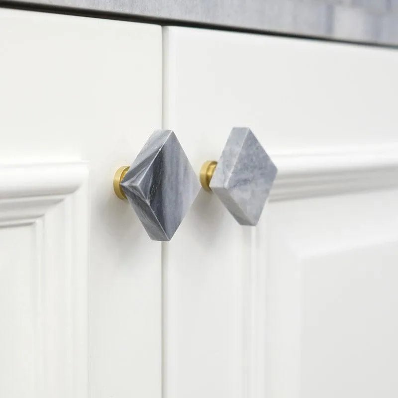 Two modern style cabinet knobs made of marble and brass, attached to a white wooden cabinet drawer, designed by Mantara