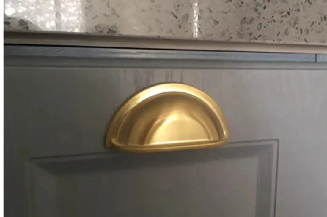 Gold-colored circular pull knob mounted on a white surface, designed for cabinets or furniture—by Mantara.