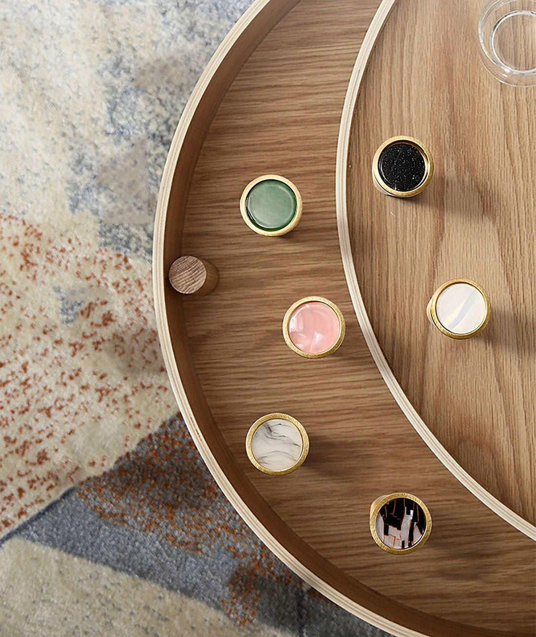 Gemstone knobs in green, white, brown, and blue mounted on a round wooden surface, showcasing vibrant style by Mantara.