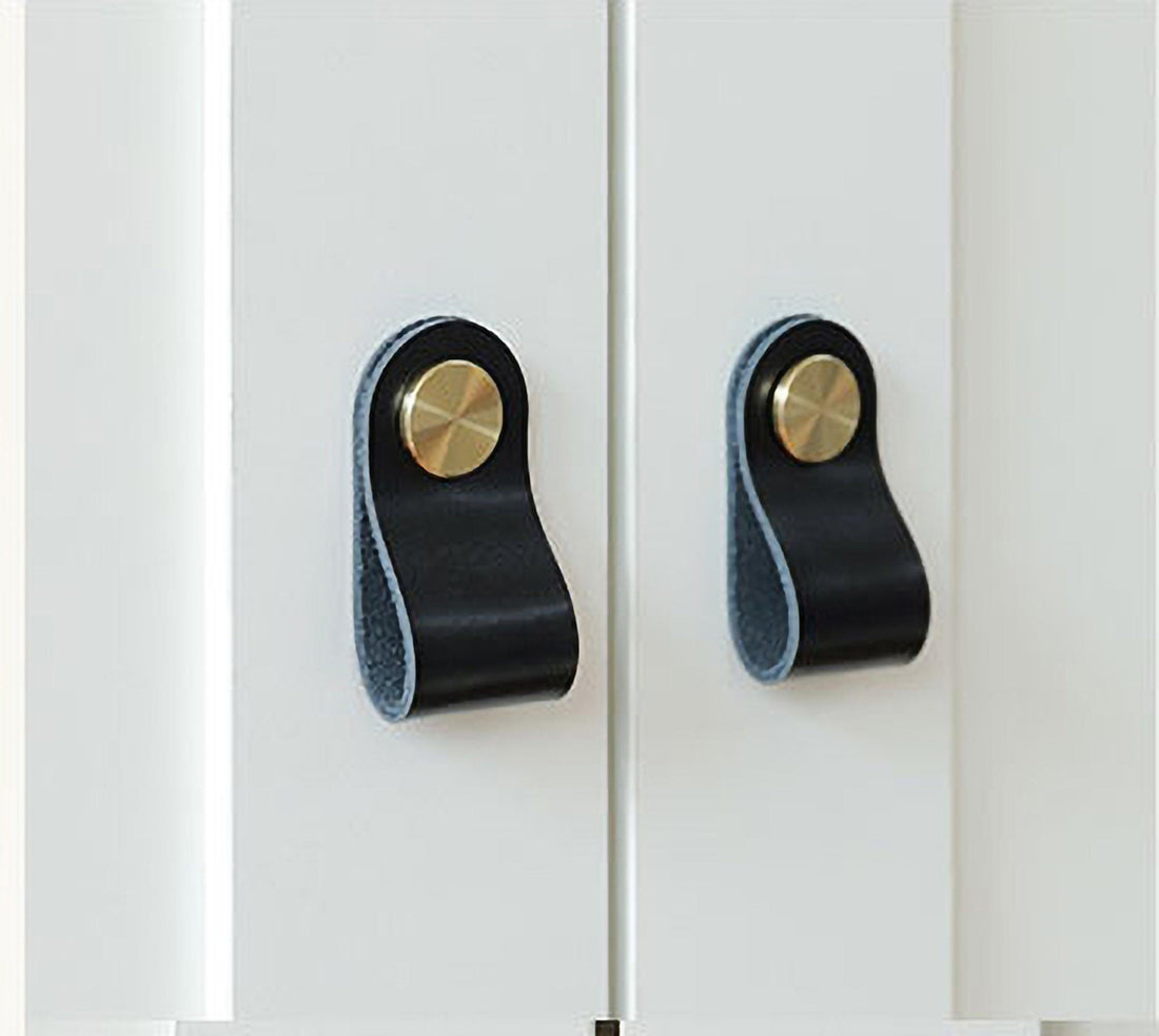 Two black and gold cabinet knobs mounted on a white cabinet surface, creating a bold, elegant contrast by Mantara.