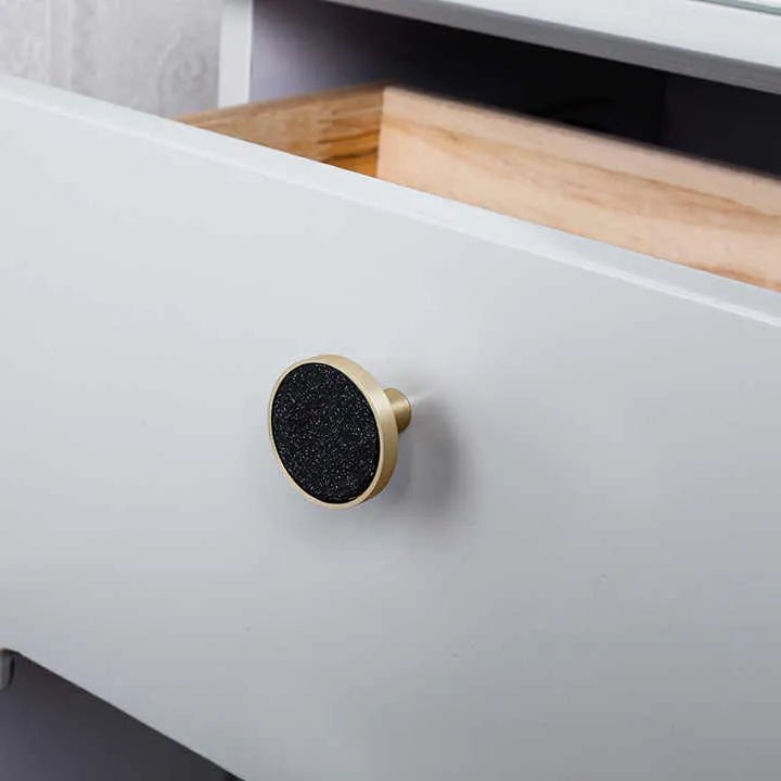 Close-up of a drawer with a gold and black knob mounted on a white cabinet, adding a bold accent by Mantara.